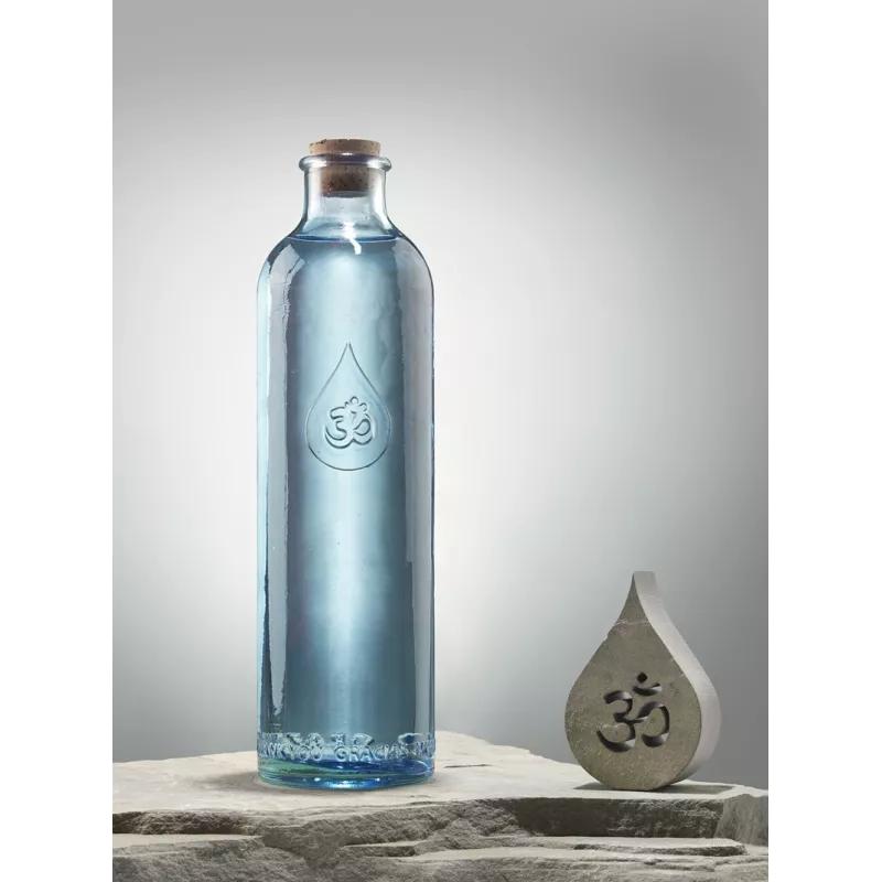 Bouteille OmWater Gratitude 1,2 L à côté d'une goutte en pierre sculptée du symbole Om