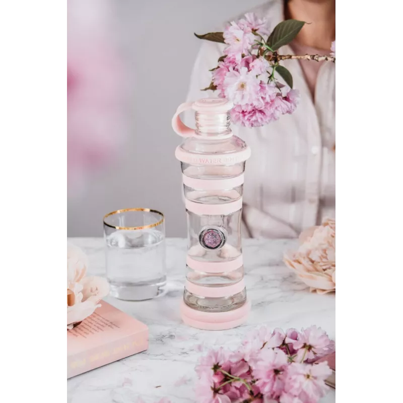 Bouteille i9 Compassion rose sur une table, entre un verre et des branches fleuries
