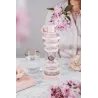 Bouteille i9 Compassion rose sur une table, entre un verre et des branches fleuries