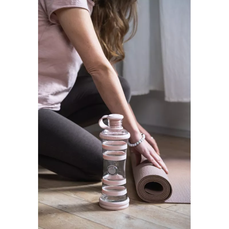 Bouteille i9 Compassion rose posée au bord d'un tapis de yoga