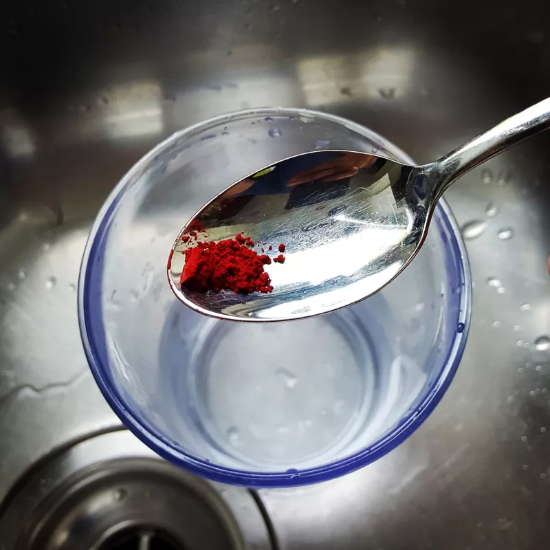 Colorant test Berkey® : de la poudre rouge sur une cuillère, au-dessus d'un bol d'eau